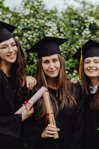 Three young female graduates in caps and gowns celebrating with diplomas outdoors.